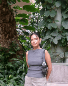 Portrait image of Juwairiyyah, who has dark brown hair tied back and is wearing a grey short sleeved shirt, carrying a black handbag.
