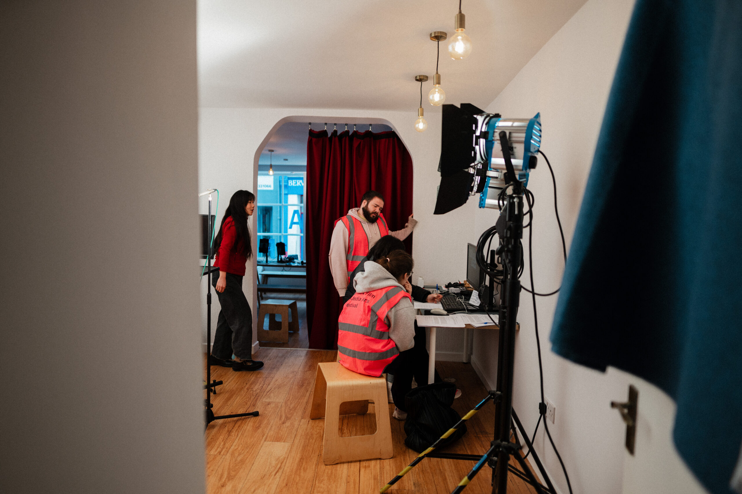 people in pink hi vis jackets looking at screens next to lighting equipment