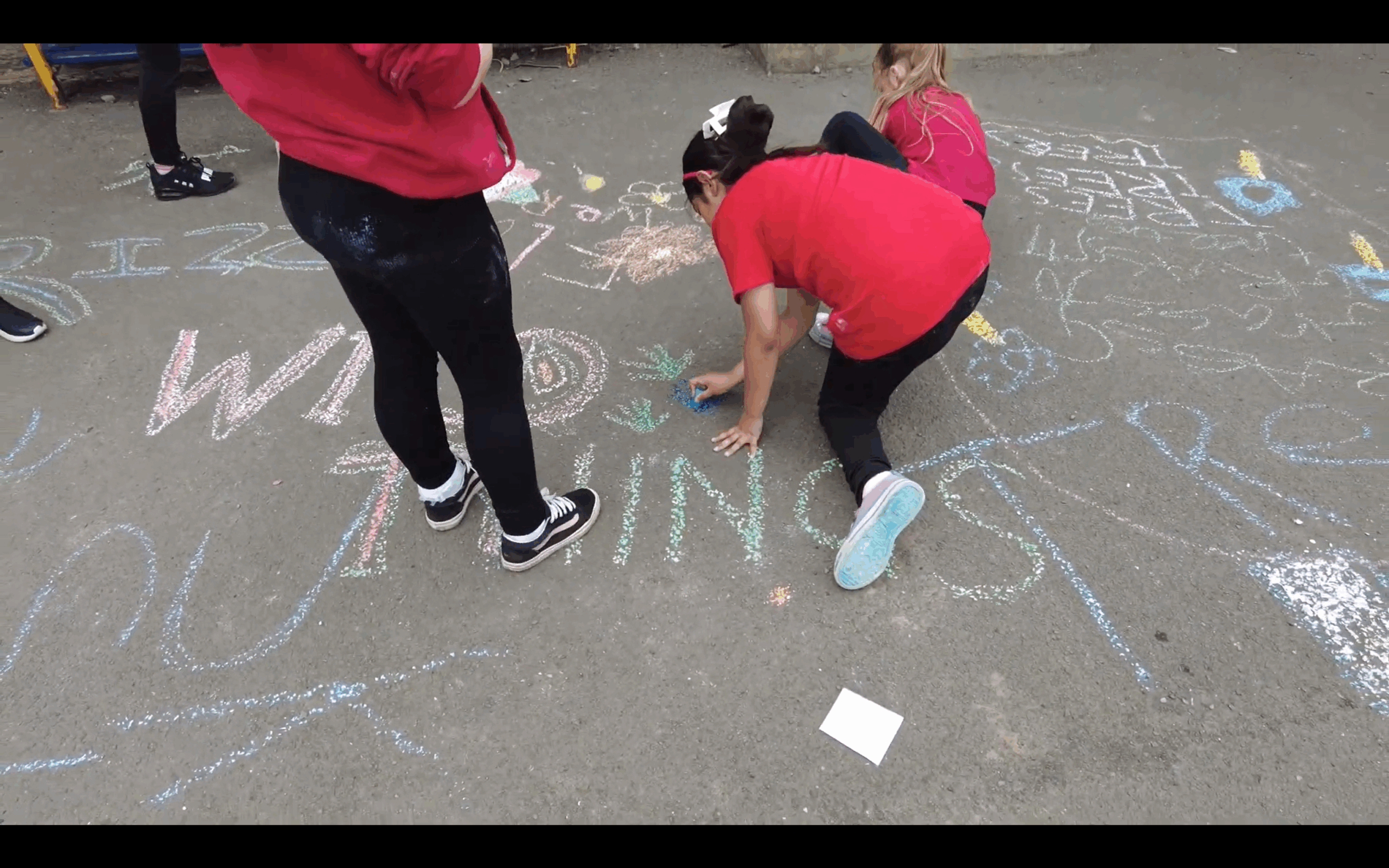 children in red shirts writing on ground in chalk