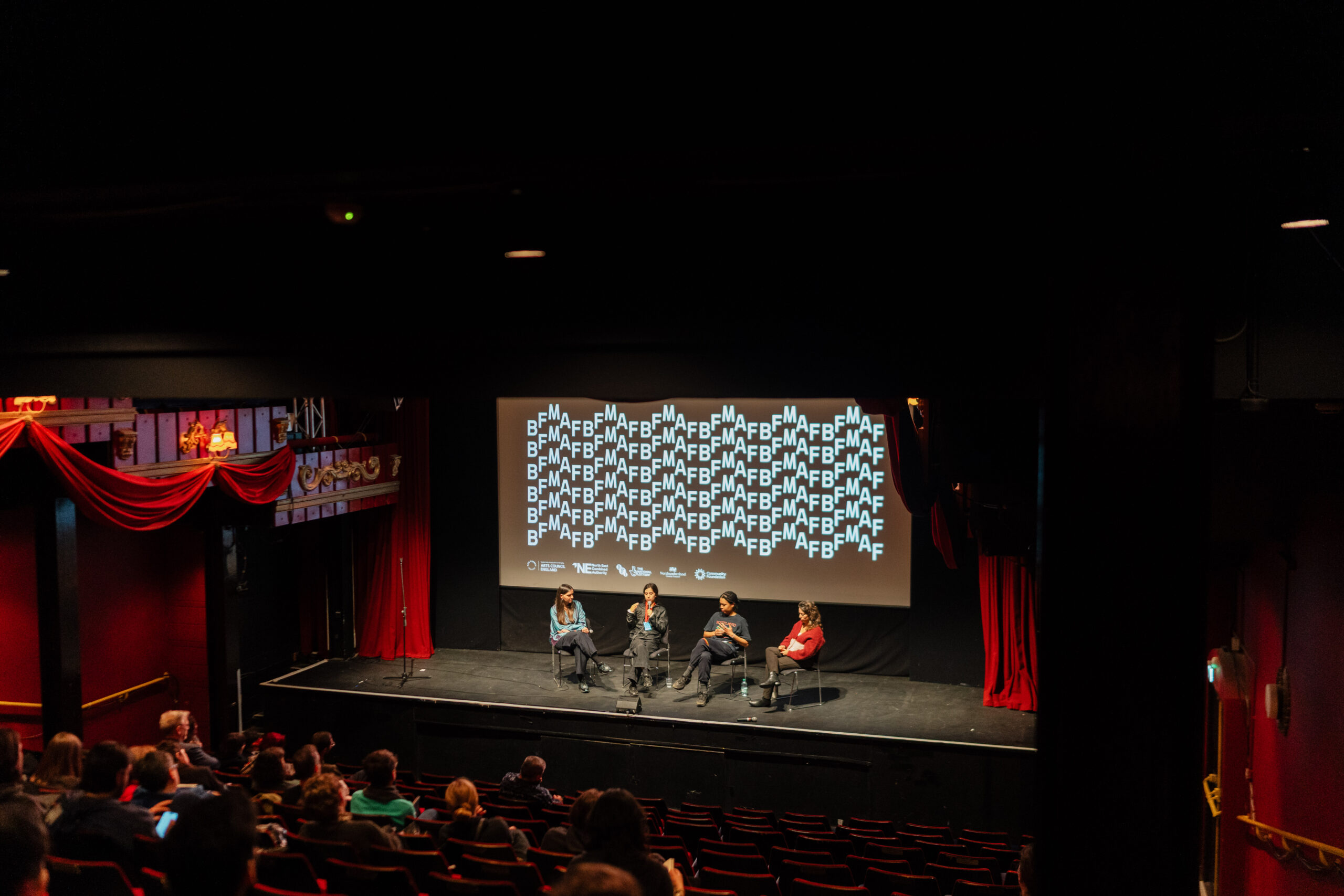 four people sat on a stage in front of a screen displaying the BFMAF logo