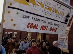 A banner held at a protest reads "Coal not Dole"