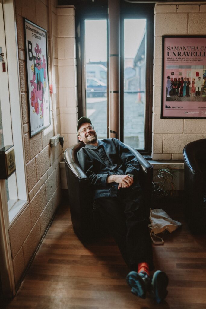 Ben Lewis sitting on a brown leather chair in the Maltings' foyer laughing