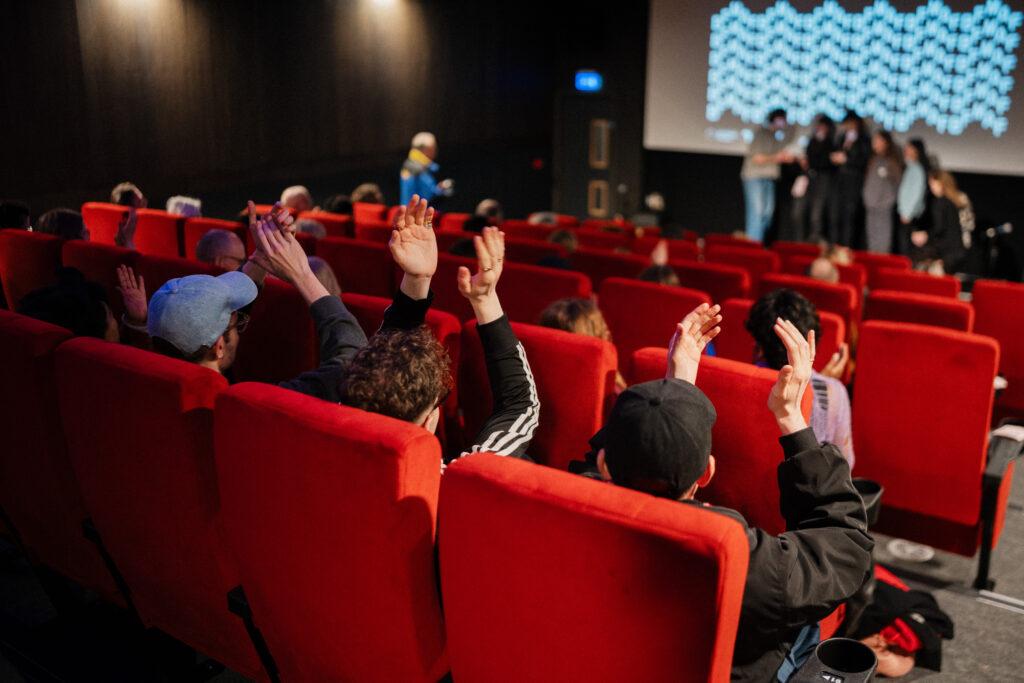 Audience members raising hands and applauding during a film festival event. Group of adults enjoying a cinema screening with positive emotions and engagement. People celebrating film culture.