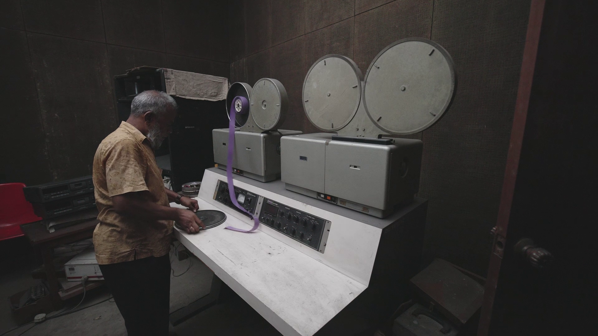 Senior adult man working with a vintage film editing machine in a dimly lit room. Old film reels and equipment highlight classic film production. Retro technology and filmmaking process.